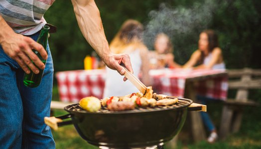 Close up of a man making barbecue and holding beer bottle.